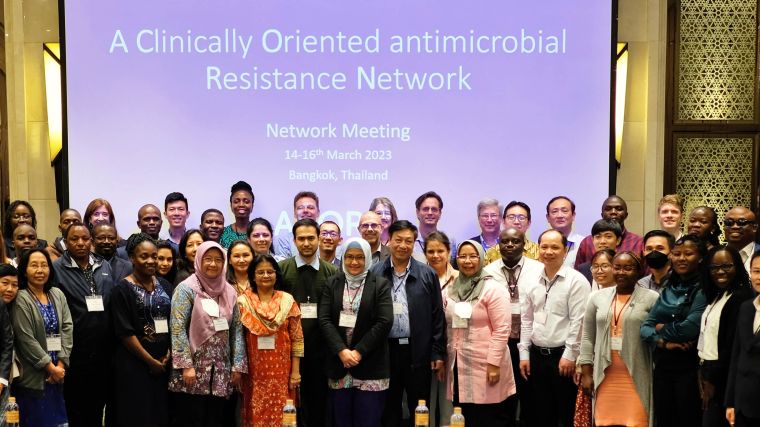 The group of people who attended the network meeting, standing in front of a screen showing the tittle 'A Clinically-Oriented antimicrobial Resistance Network'