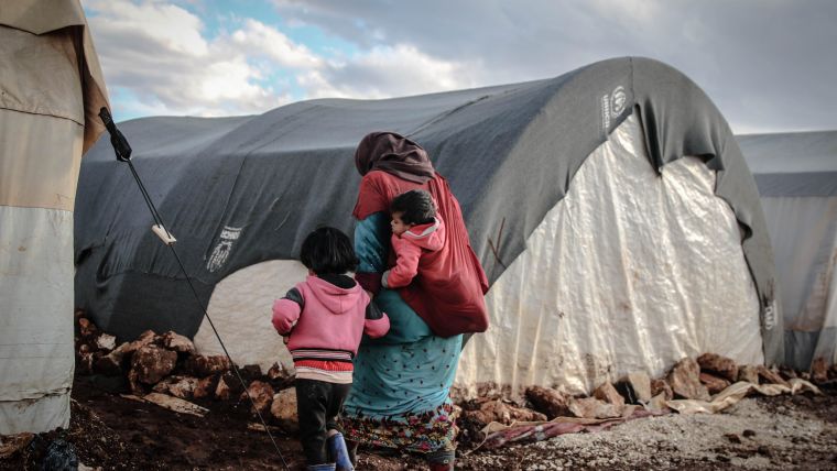 Photo of a mother and two young children in a tented refugee camp