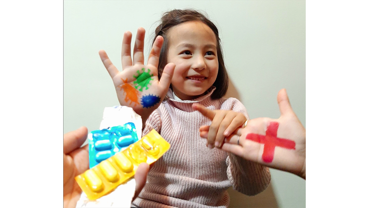 Child showing coronaviruses drawn on her hand, with pills, and a red cross drawn on a adult hand