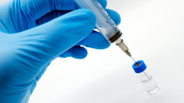 Gloved hand holding a syringe inserted into a small vial