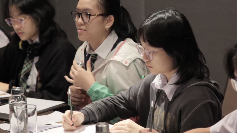 Screenshot of the video 'Three-minute thesis competition' showing students taking notes during the competition